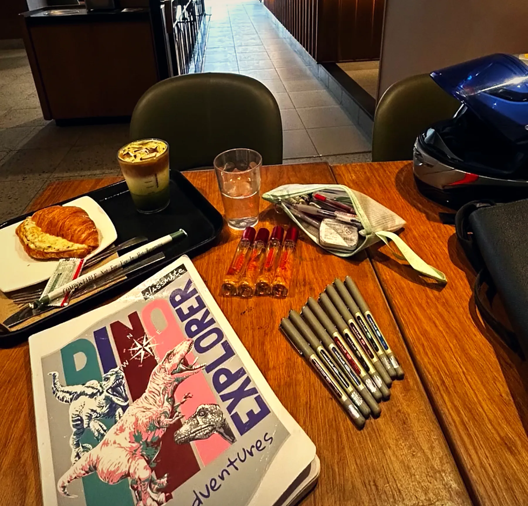 A café table with a latte, a croissant, a notebook and marker pens