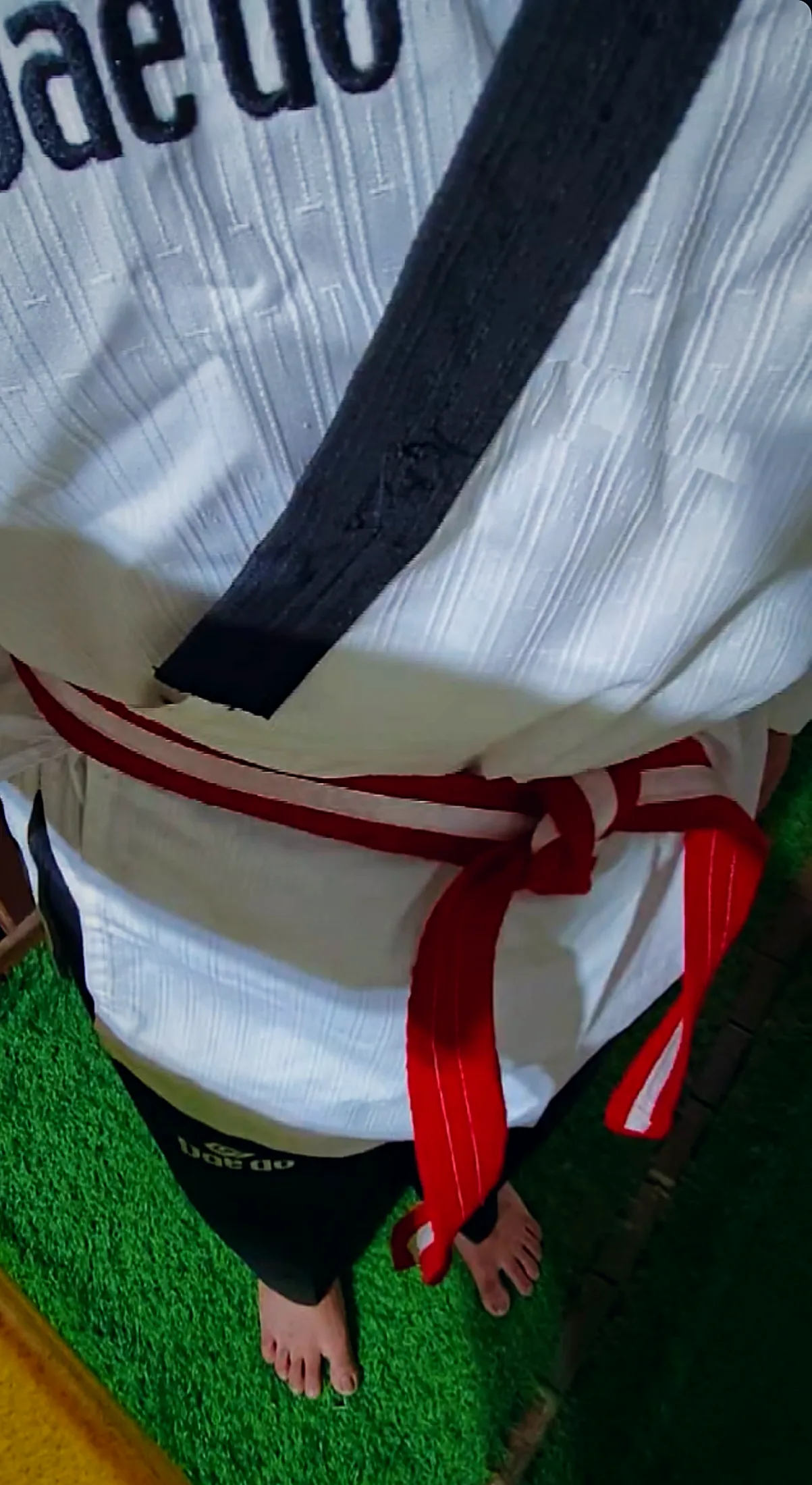 Looking down at a Daedo dobok with a black collar and a belt tied at the waist