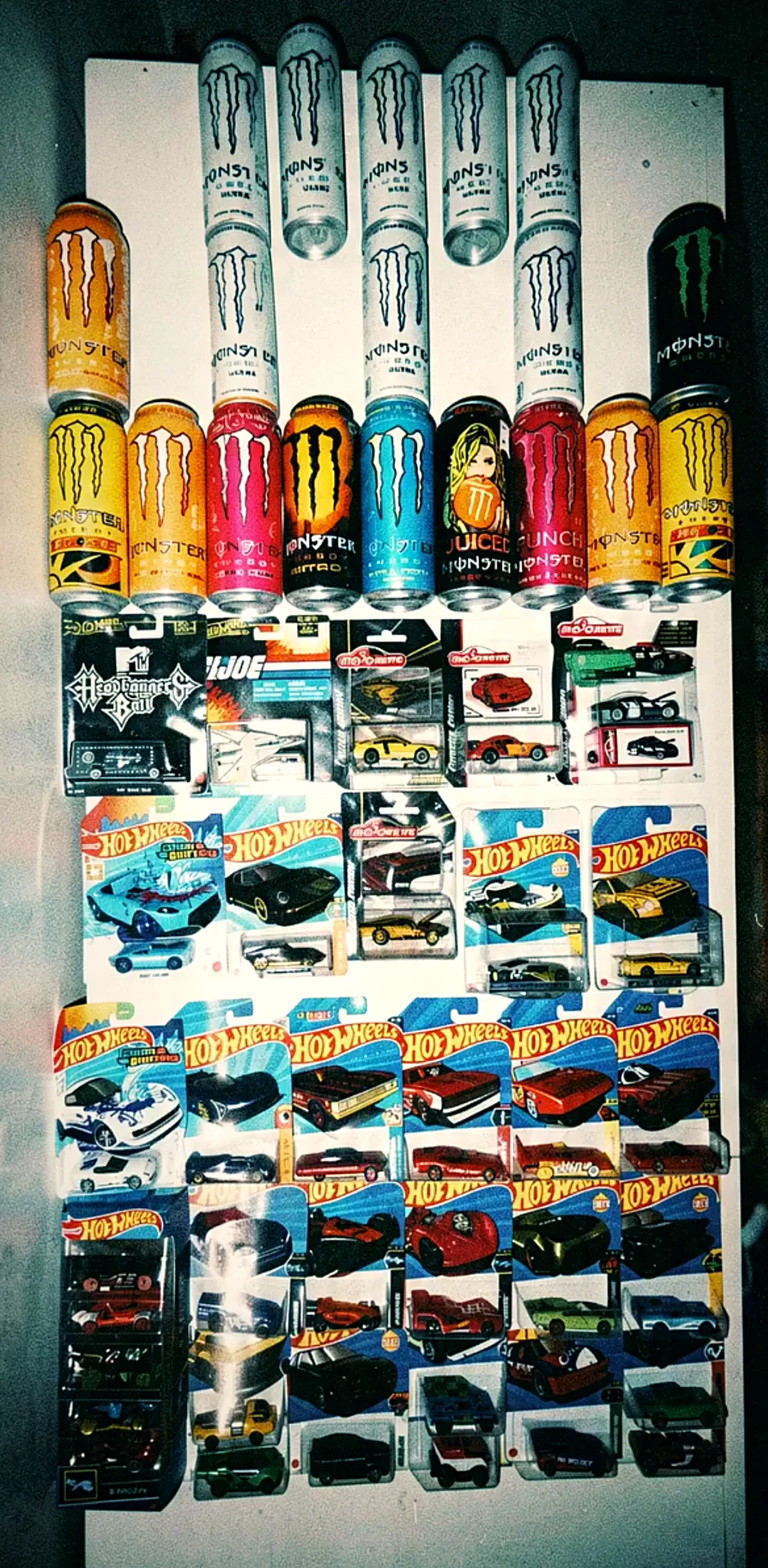 A shelf of boxed Hot Wheels cars below a row of energy-drink cans